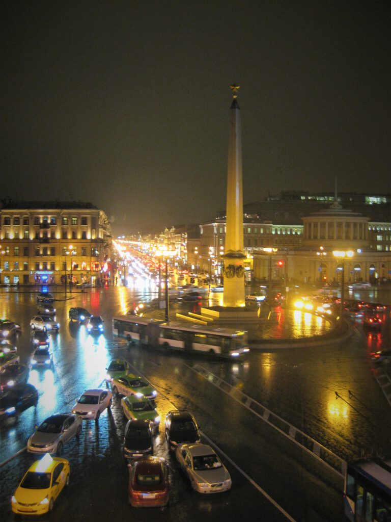 Kreisel mit Helden-Obelisk in St. Petersburg. Bei Nacht mit viel Verkehr.