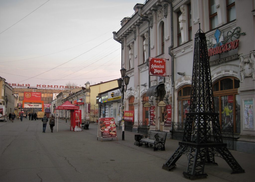 Fußgängerzone in Irkutsk. Viele rote Schilder. Rechts ein Miniatur-Eiffelturm. 