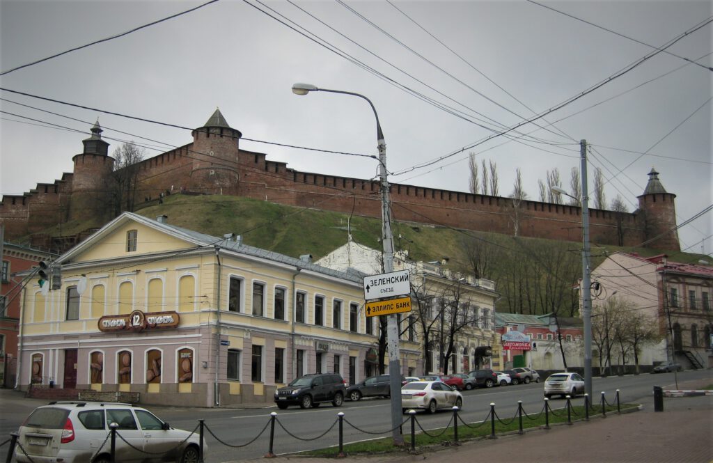 Kremlmauern auf grünem Hügel hinter klassizistischem, gelbem Gebäude an Hauptstraße. 