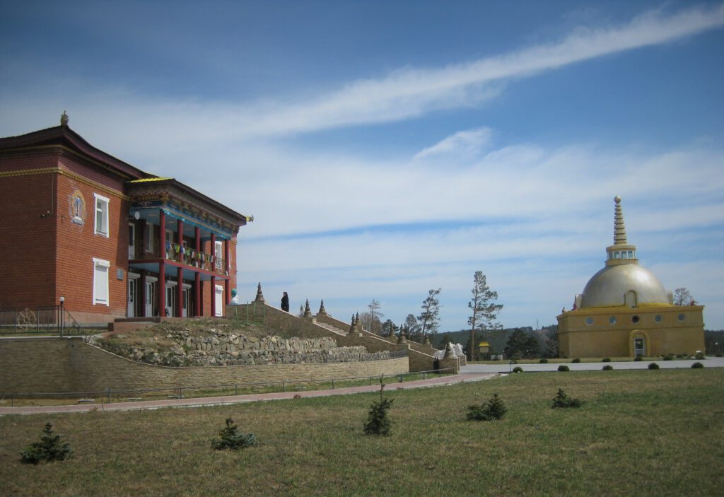 Dazan Rinpotsche Bagscha. Links das Klostergebäude. Rechts die goldene Stupa. Vorne Rasen. 