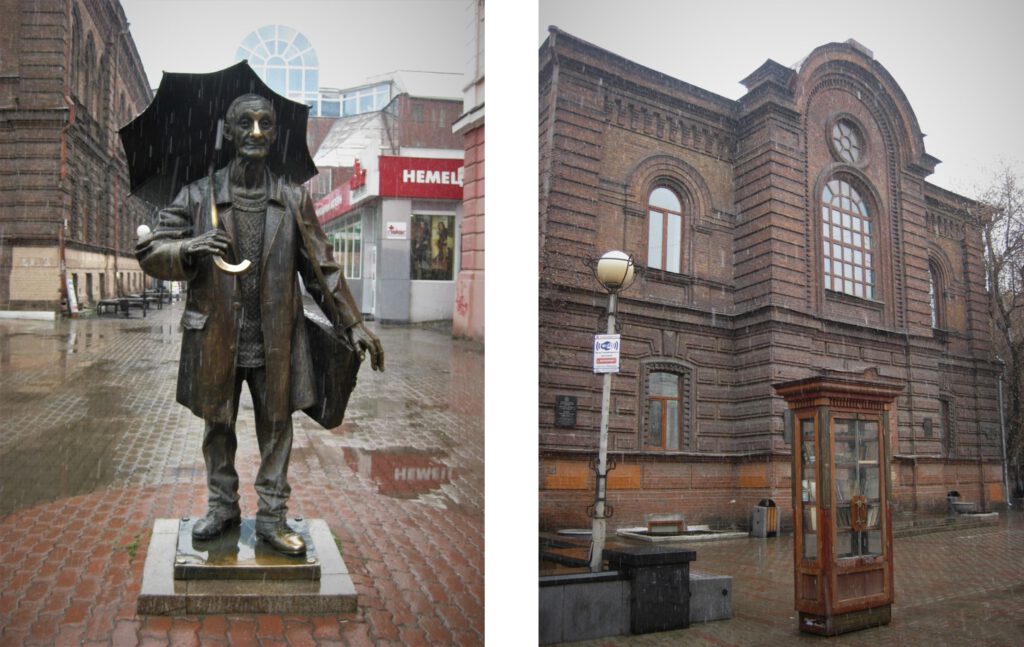 Krasnojarsk; Bronzemann im Regen. Skulptur mit Regenschirm hinter dem Kopf. Rechts ein Universitätsgebäude. 