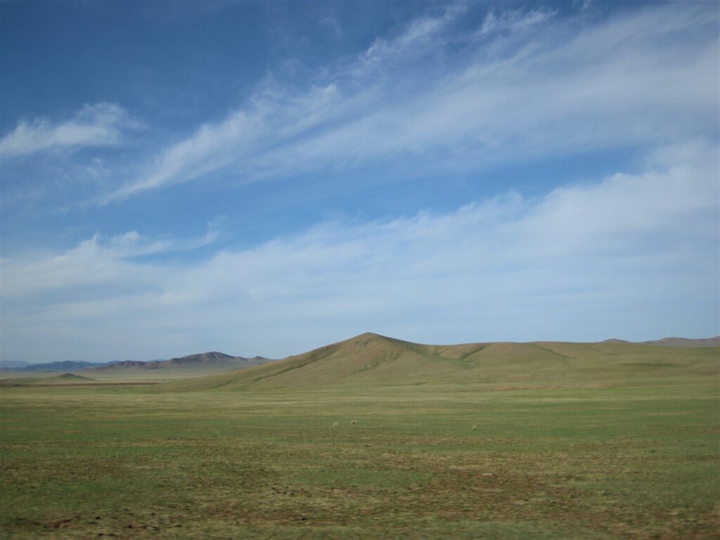 Weite mongolische Steppe mit kleineren begrünten Hügeln. 