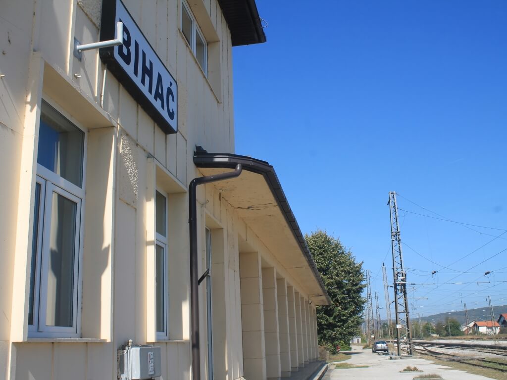 Bahnsteig vor beigfarbener Fassade des Bahnhofs von Bihac. 