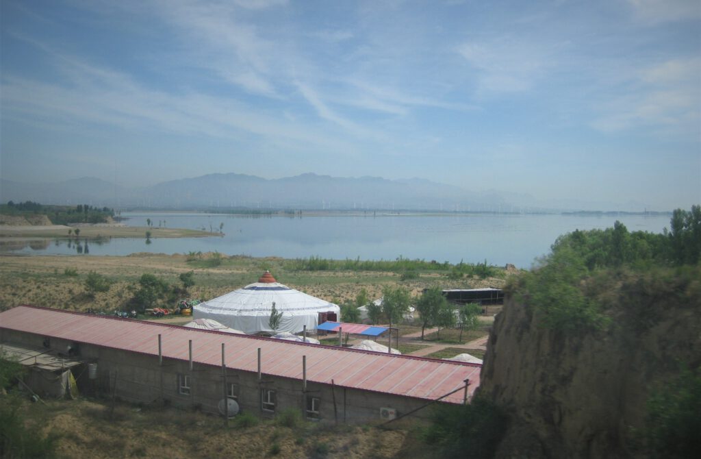 Blick über einen See in der Inneren Mongolei. Im Vordergrund eine weiße Jurte, 