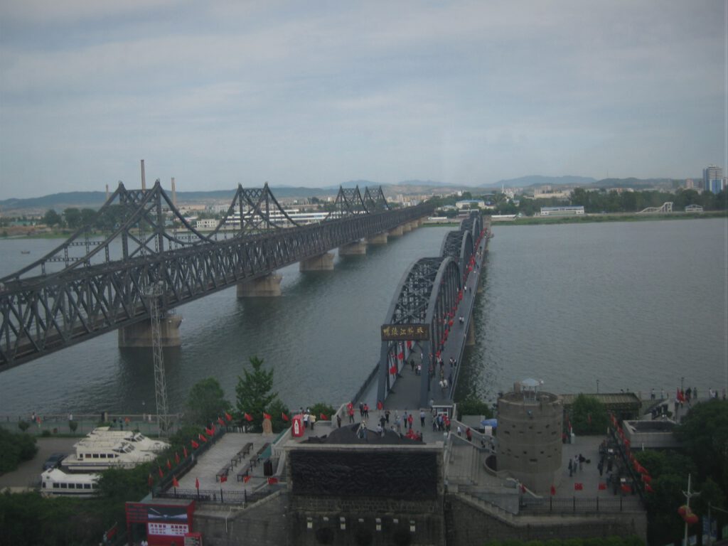 Blick über die zwei Yalu-Brücken nach Nordkorea. Links die sino-koreanische Freundschaftsbrücke. Rechts die gebrochene Brücke. 
