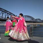 Brücke nach Nordkorea. Frauen in pinkfarbenen, traditionellen Kleidern vor der chinesisch-koreanischen Freundschaftsbrücke in der Grenzstadt Dandong.
