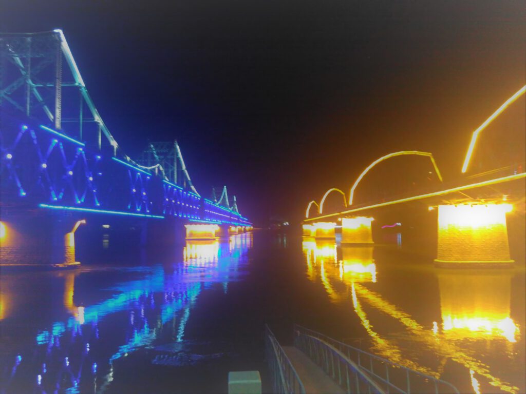 Die Freundschaftsbrücke ist nachts blau beleuchtet, die gebrochene Brücke ist gelb beleuchtet.