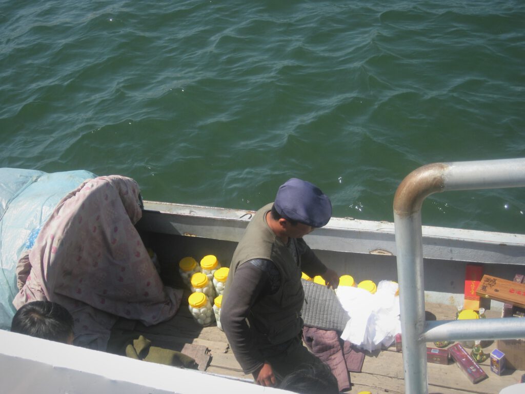 Nordkoreanischer Verkäufer im Boot auf dem Yalu Fluss. Er verkauft unter anderem eingelegte Eier und Zigaretten. 