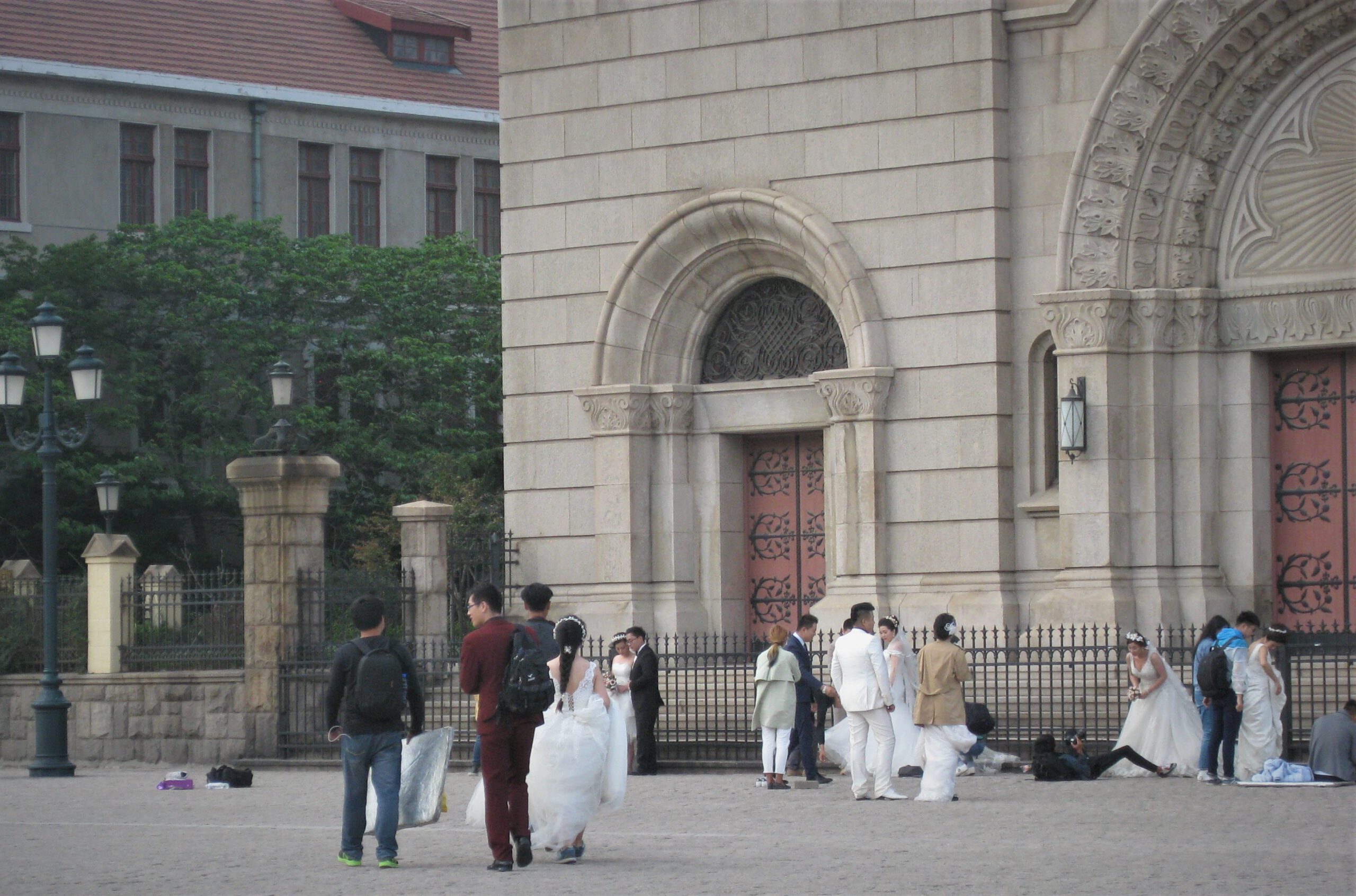 Mehrere Brautpaare mit Fotografen auf dem Platz vor der Kathedrale. Bräute in weißen Brautkleidern. Bräutigams im Anzug.  