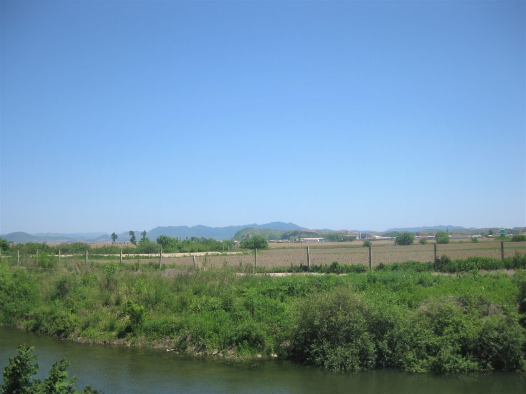 Blick über enge Stelle des Yalu Fluss Richtung Nordkorea. Nur ein kleiner Zaun steht auf nordkoreanischer Seite der Grenze. 
