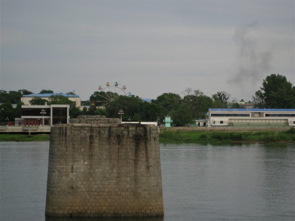 Restliche Pfeiler der gerbochenen Brücke im Yalu. Im Hintergrund das Ufer von Sinuiju mit dem Riesenrad.