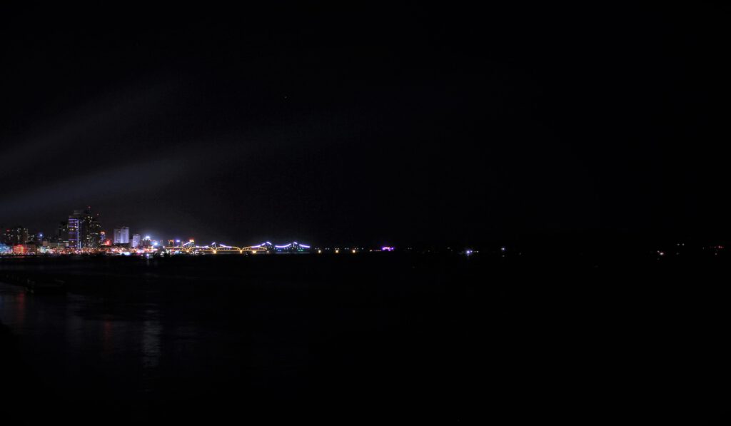 Nachtaufnahme von Dandong von Süden aus. In der Ferne die hell beleuchteten Brücken, nur auf chinesischer Seite beleuchtet.