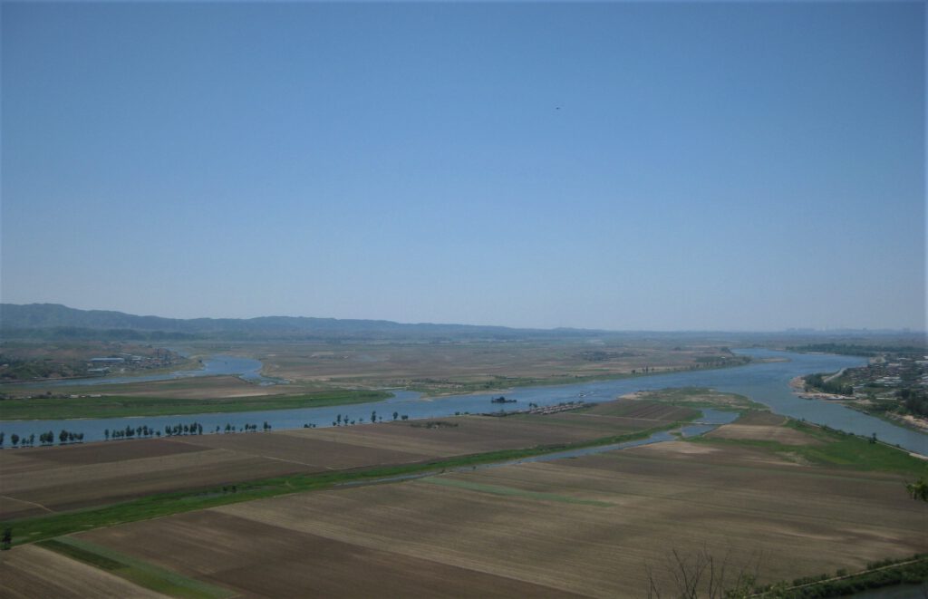 Das Yalu-Flussbecken am Tigerberg. Verzweigte Flussarme zwischen Feldern, unter bleuem Himmel.
