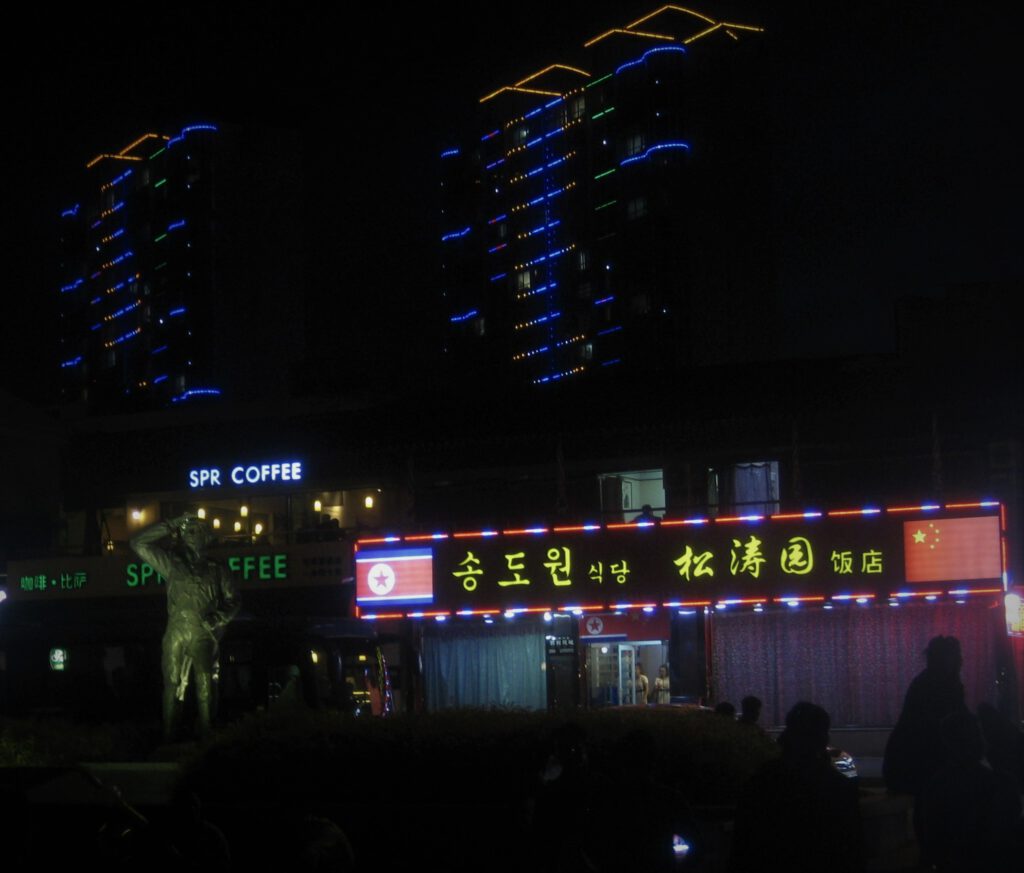 Ein nordkoreanisches Restaurant in Dandong. Im Hintergrund beleuchtete Hochhäuser von Dandong.