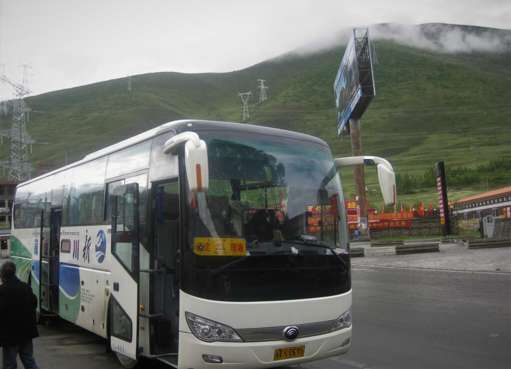 Moderner Reisebus bei einer Pause vor einem grünen Hügel in Sichuan.