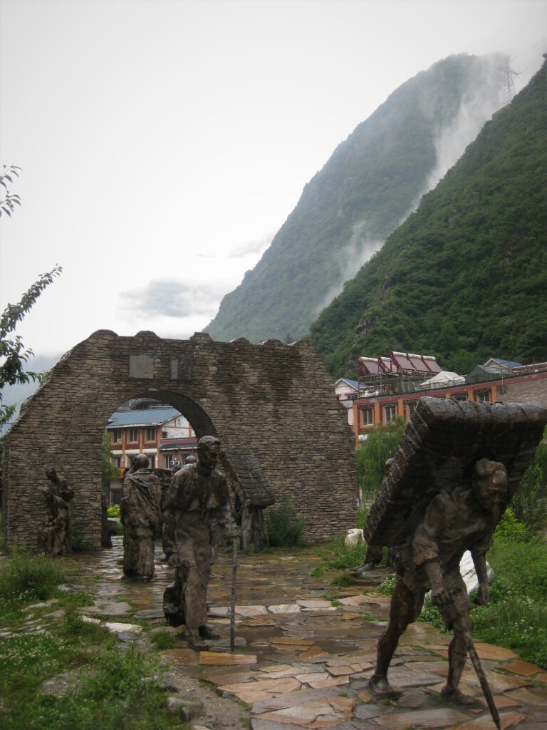 Mehrere Bronzefiguren vor dem alten Stadttor von Kangding. Im Hintergrund die vernebelten Berge. 