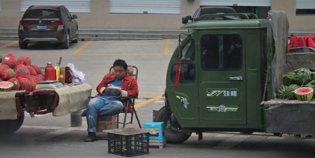 Chinesischer Straßenverkäufer zwischen zwei Lastwagen mit Melonen