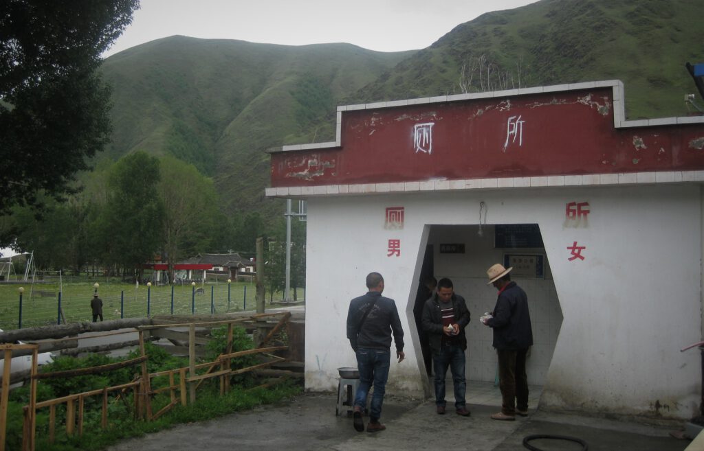 Drei Männer vor einer öffentlichen Toilette in Sichuan. 