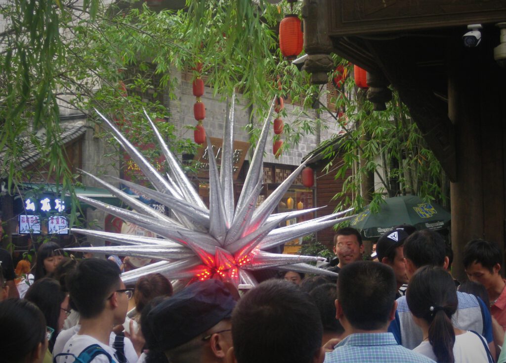 Menschentraube in der Jinli Street in Chengdu. In der Mitte ein Mann im Kostüm eines Außerirdischen. 