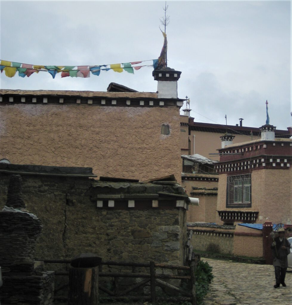 Häuserfassaden vor dem Geburtshaus des 7. Dalai Lama in Litang. Mann mit Gebetsmühle. 