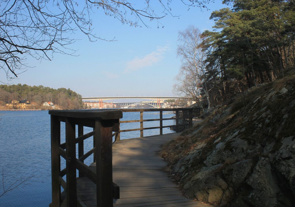 Holzsteg an der Westküste Stora Essinges entlang der Oxhålt Enge. Im Hintergrund zwei Brücken Stockholms: Alviksbron und Tranebergsbron. 
