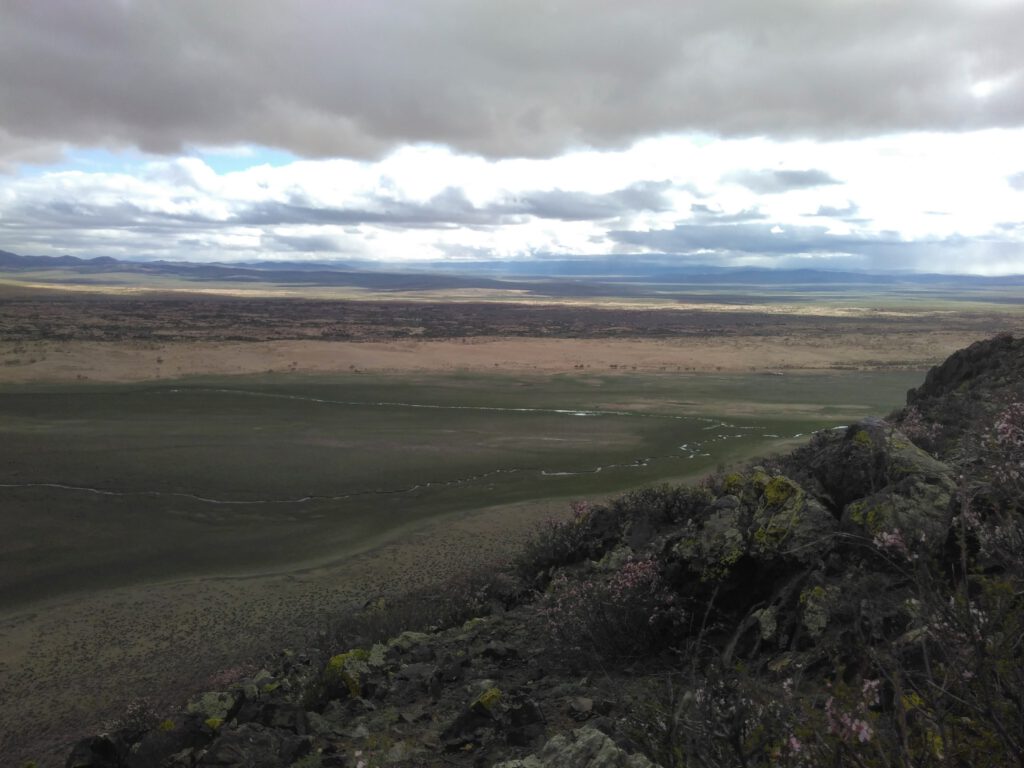 Blick von einem Berg über die Weite der Landschaft mit ihren wechselnden Zonen. Grasland, Wüste, Steppe. Es ist bewölkt. 