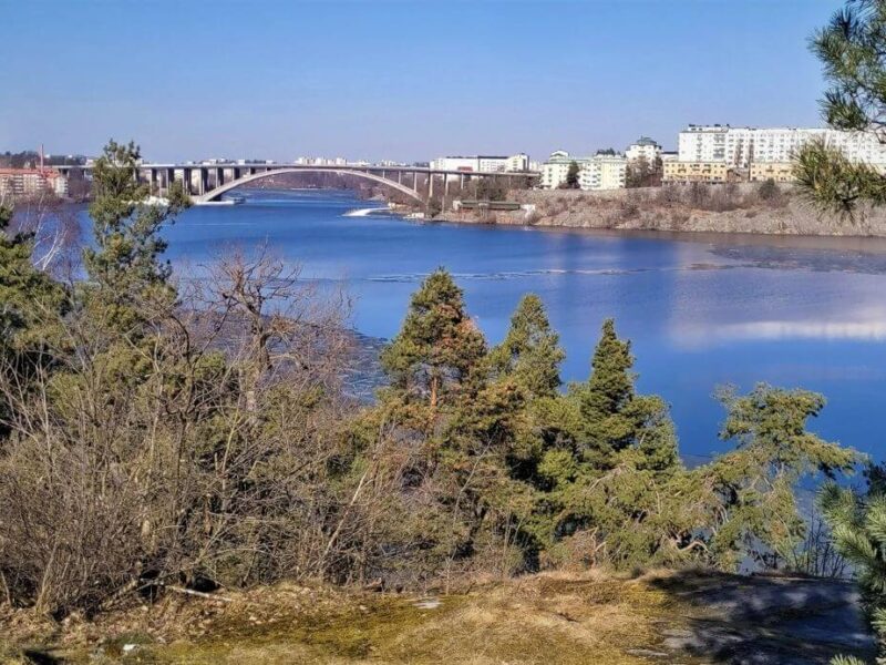 Stockholm zu Fuß erkunden - mit Aussicht. Die Brücke Tranebergsbron in Stockholm von der Insel Stora Essingen aus. Blick über die Bucht Essingefjäreden des Mälarsees. East Rail Stories