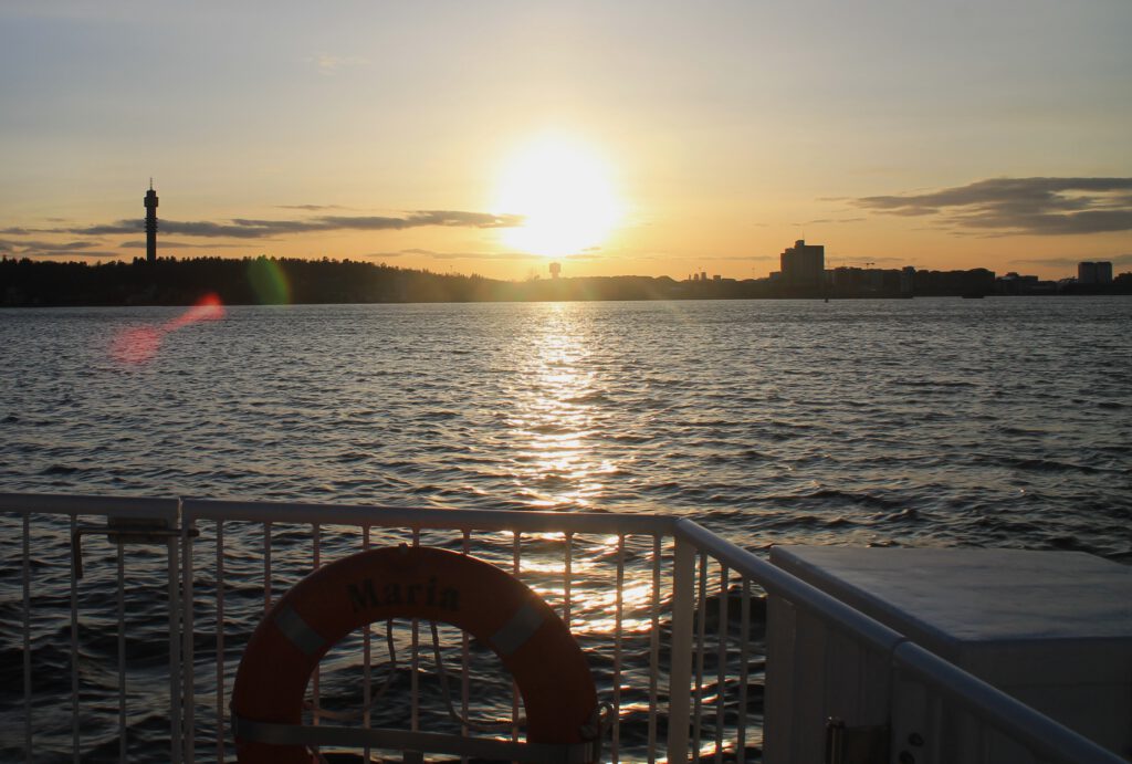 Foto gegen die Sonne über das Wasser zur Küste des Djurgården. Links der Fernsehturm Kaknästornet. Fotografiert gegen die untergehende Sonne. 