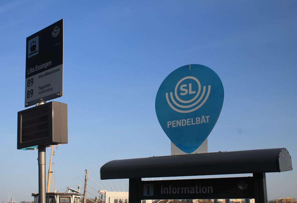 Nahaufnahme Haltestellen-Schild Pendelbat Linie 89 in Lilla Essingen. Rechts hellblaues tropfenförmiges Schild mit Logo der SL und Aufschrift Pendelbat.  