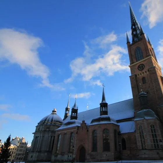 Kirchturm der gotischen Begräbniskirche Riddarsholmkyrkan ragt in den blauen Himmel. Dach den Kirchenschiffs schneebedeckt. Stockholm 2022