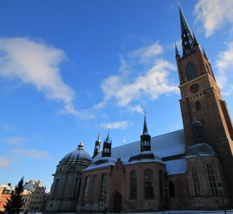Kirchturm der gotischen Begräbniskirche Riddarsholmkyrkan ragt in den blauen Himmel. Dach den Kirchenschiffs schneebedeckt. Stockholm 2022