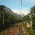 Mit dem Zug nach Venedig. Zweispurige Eisenbahnschienen zwischen den alpinen Gebirgen. Rechts rote Ampel, links grüne Ampel. Im Hintergrund schneebedeckter Berg in den Alpen.