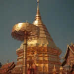 Wat That Doi Suthep. Goldene Chedi mit goldenen Statuen und Sonnenschirm. Chedi ist von Zaun umgeben.