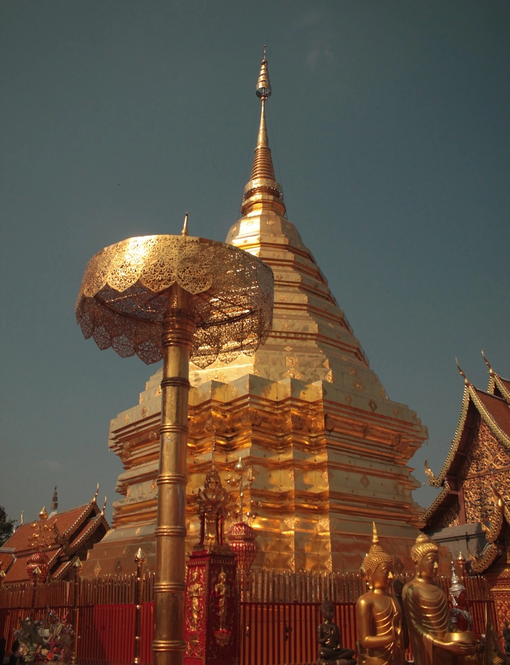 Wat That Doi Suthep. Goldene Chedi mit goldenen Statuen und Sonnenschirm. Chedi ist von Zaun umgeben.