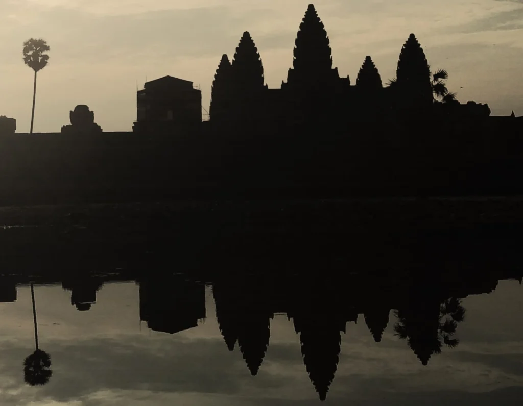 Tempel Angkor Wat in Kambodscha. Die 5 Türme spiegeln sich im ruhigen Wasser eines Teiches. Eine Palme auf der linken Seite vervollständigt das malerische Bild. Schwarz weiß mit starkem Kontrast.