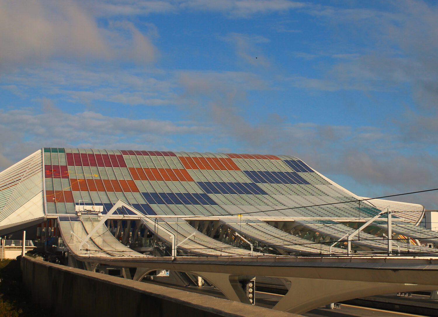 Blick auf das Dach des Bahnhofs Liege-Guillemins von der südlichen Rückseite. Blaue, rote, orange und grüne Quadrate verlaufen diagonal über das Dach.