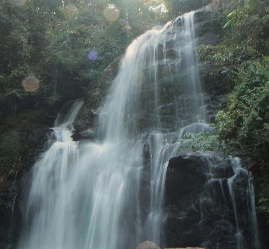 Nahaufnahme des Pha Dok Siew-Wasserfalls im Doi Inthanon Nationalpark in Thailand. Das Wasser stürzt in mehrere kleine Kaskaden über Felsen und bildet sprühende Gischt. Umgeben von dichtem Dschungel und moosbedeckten Steinen ist der Wasserfall ein beeindruckendes Naturwunder.