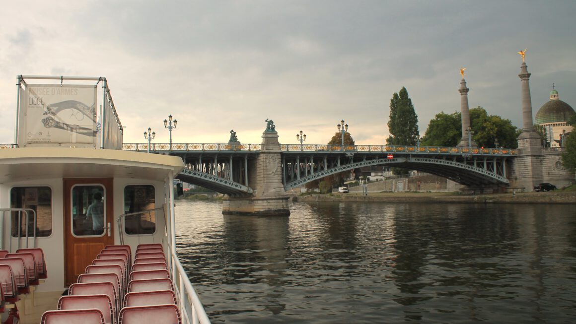 Liege: Bootsfahrt auf der Maas. Offenes Boot auf der Maas vor der Engelsbrücke in Lüttich. Boot is menschenleer. Bewölkter Himmel.