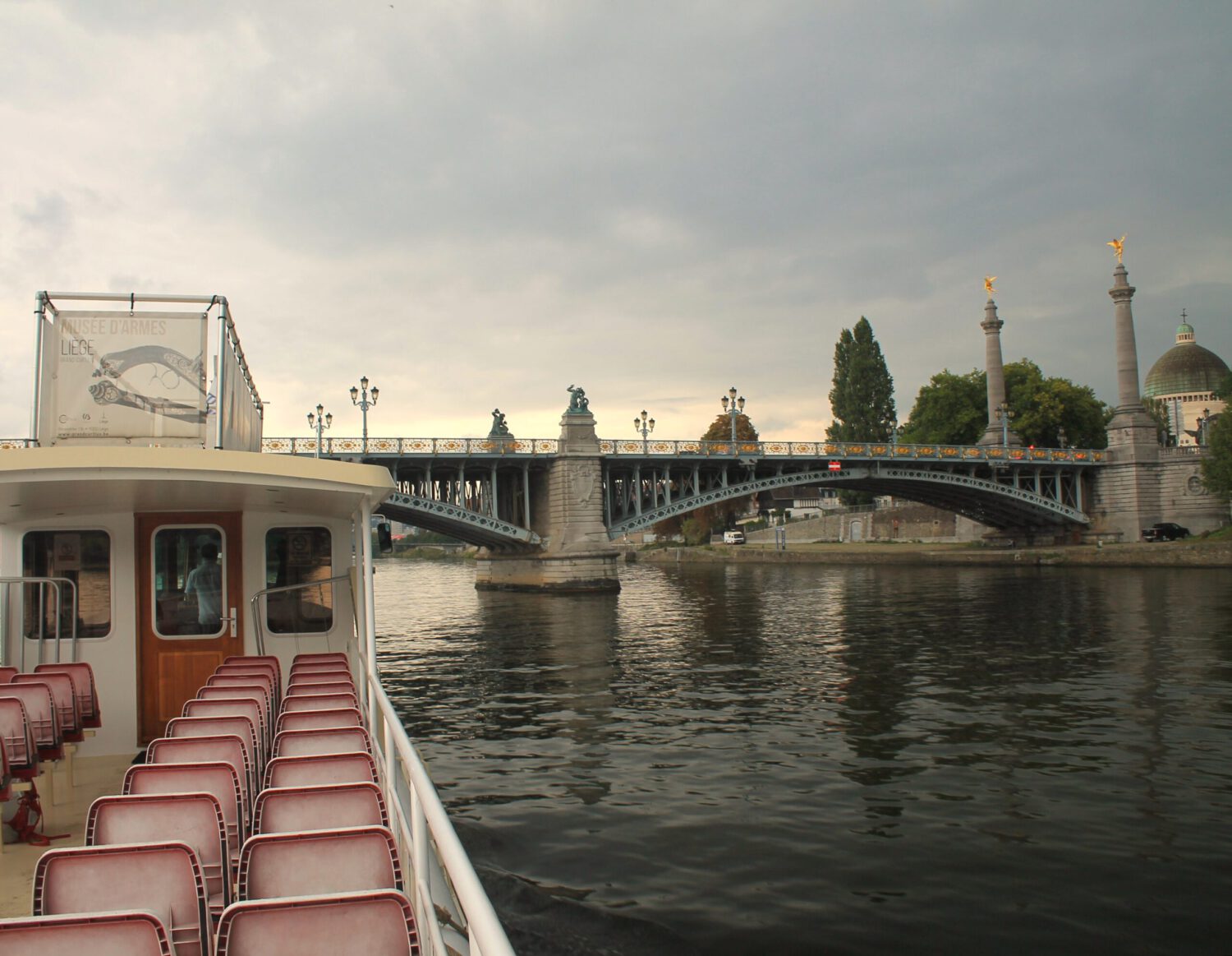 Liege: Bootsfahrt auf der Maas. Offenes Boot auf der Maas vor der Engelsbrücke in Lüttich. Boot is menschenleer. Bewölkter Himmel.