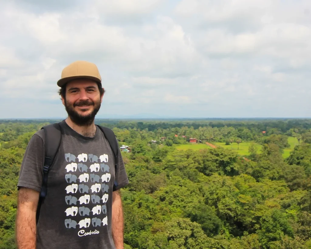 Ich mit Cap und Elefanten-T-Shirt vor grüner Landschaft von Koh Ker. Bewölkter Himmel.
