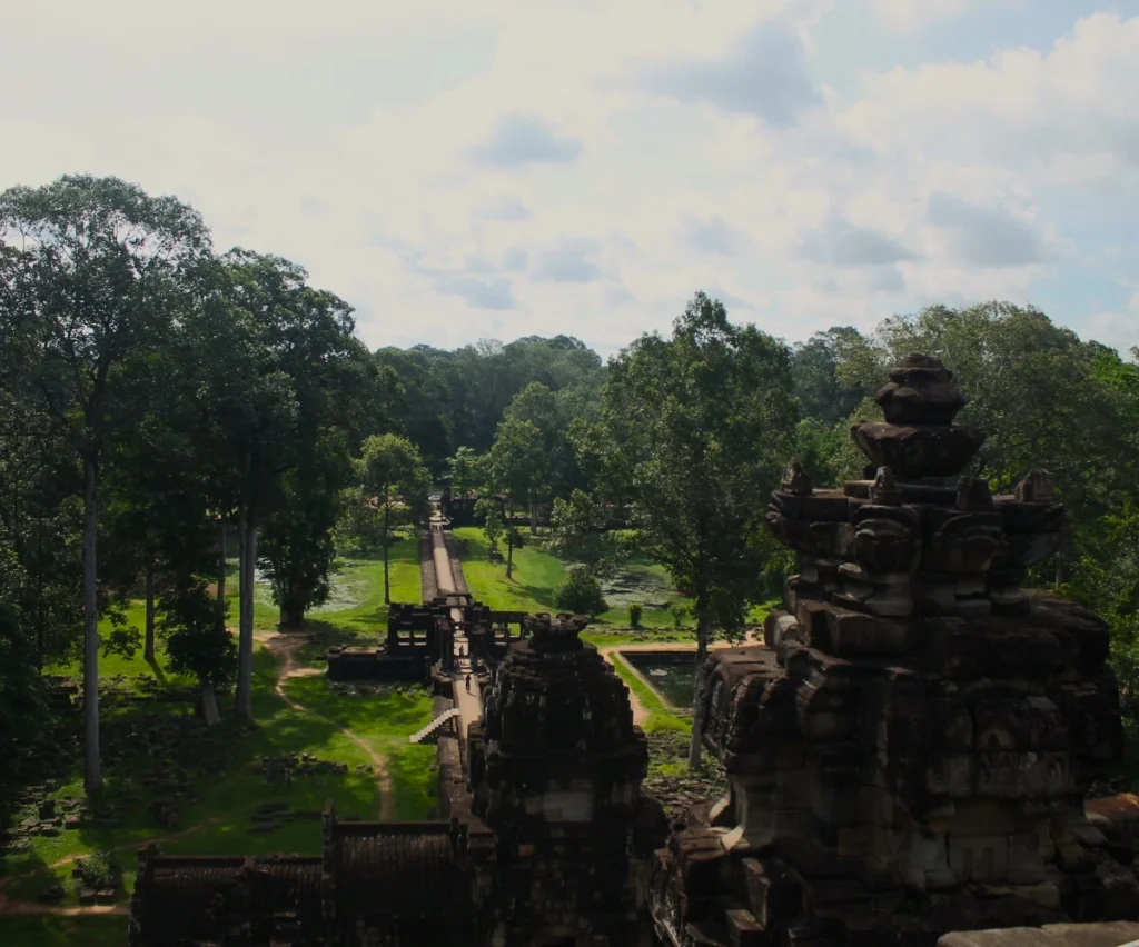 Ästhetik im Khmer-Reich. Ausblick vom Tempelberg Baphuon in Angkor Thom auf 172 m langen Steg. Steg verläuft durch Grünfläche mit Rasen und Bäumen. Im Vordergrund Türme des Baphuon-Tempels.