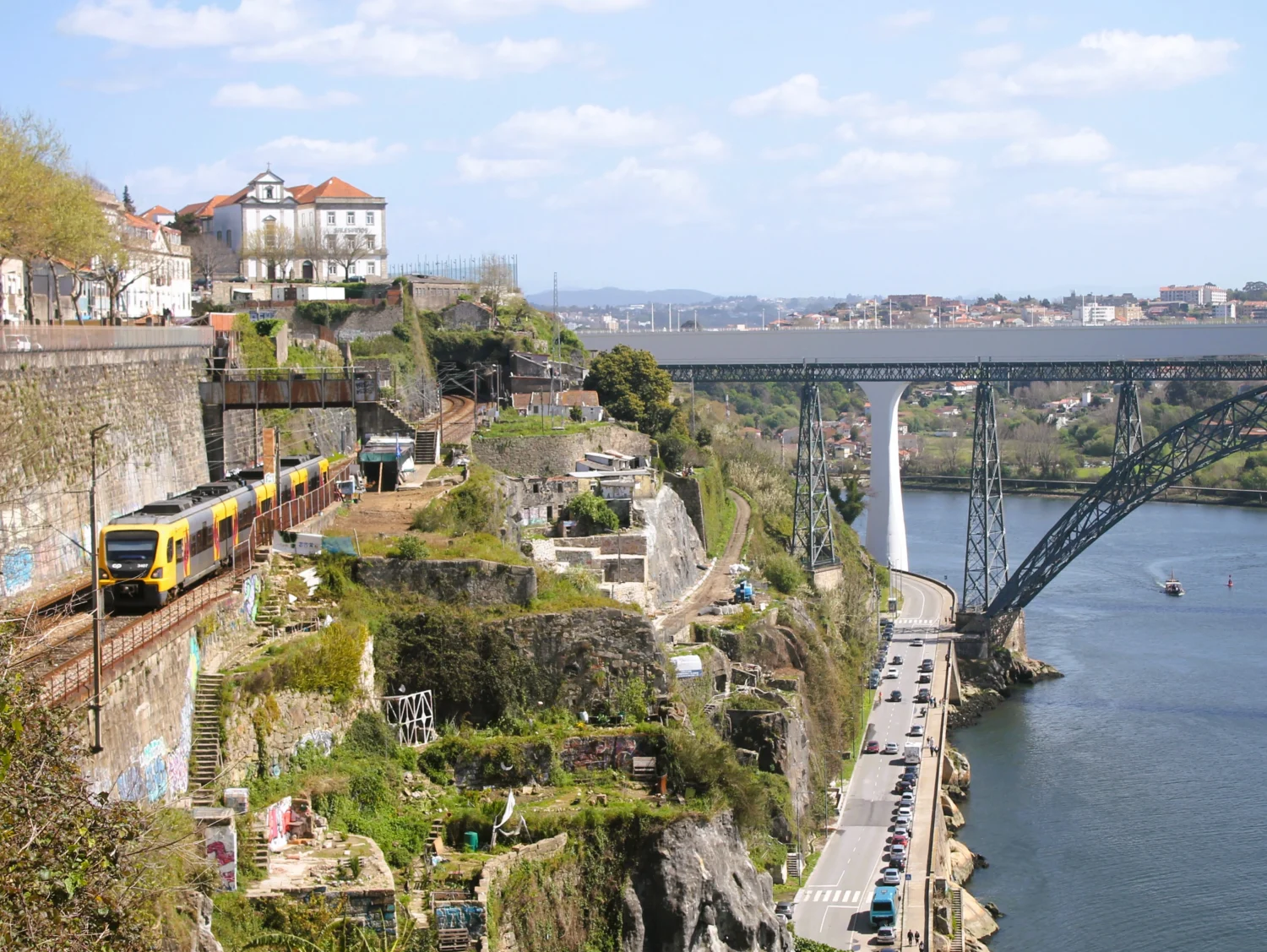 Regionalzug fährt entlang des Steilhangs von Porto. Im Hintergrund Brücken über den Douro.