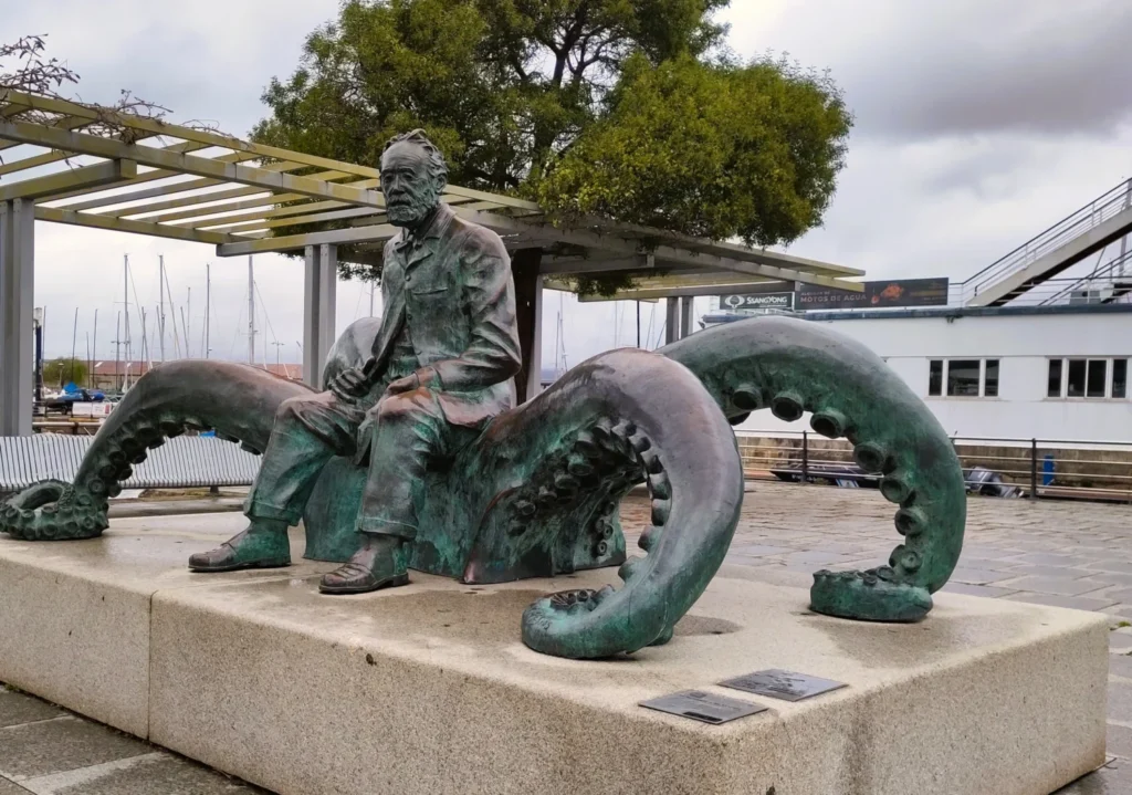 Bronzestatue von Jules Verne, sitzend auf einer Krake. Weise blickend.
