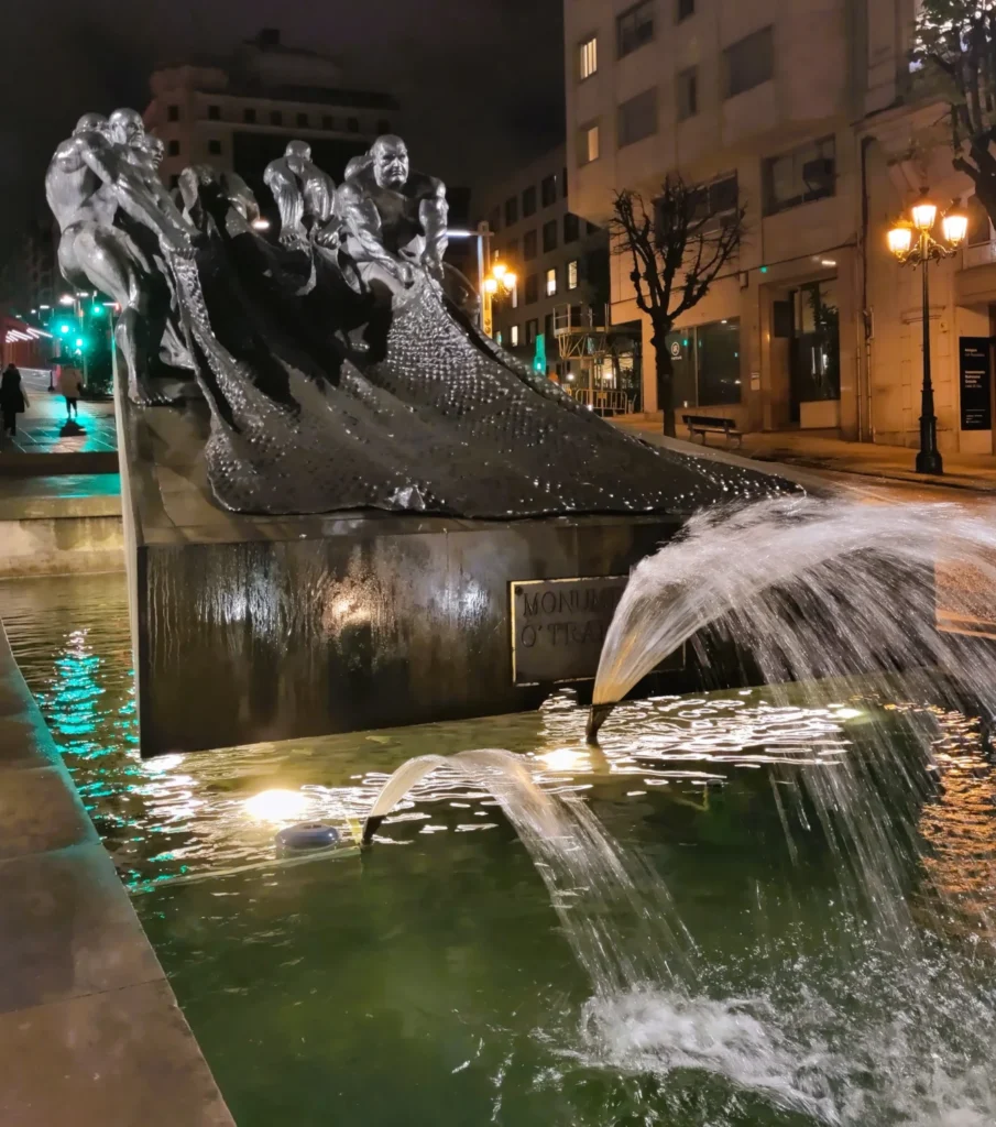 Skulptur Monumento ao Trabalho bei Nacht: Mehrere muskulöse Männer ziehen an einem Fischernetz. Darunter beleuchtete Wasserfontänen.