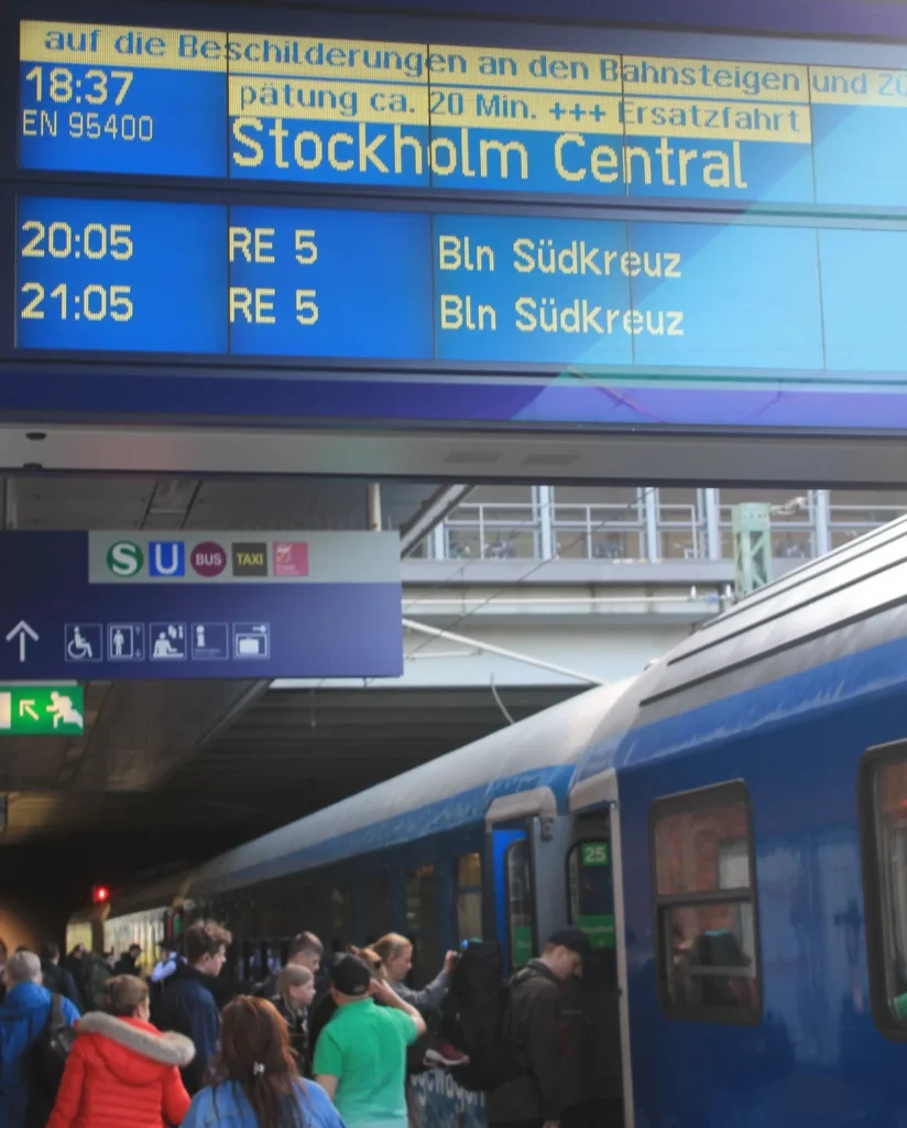 Passagiere steigen in den Nachtzug. Die Anzeige am Bahnsteig zeigt 20 Minuten Verspätung an. Planmäßige Abfahrt nach Stockholm Central um 18:37. 