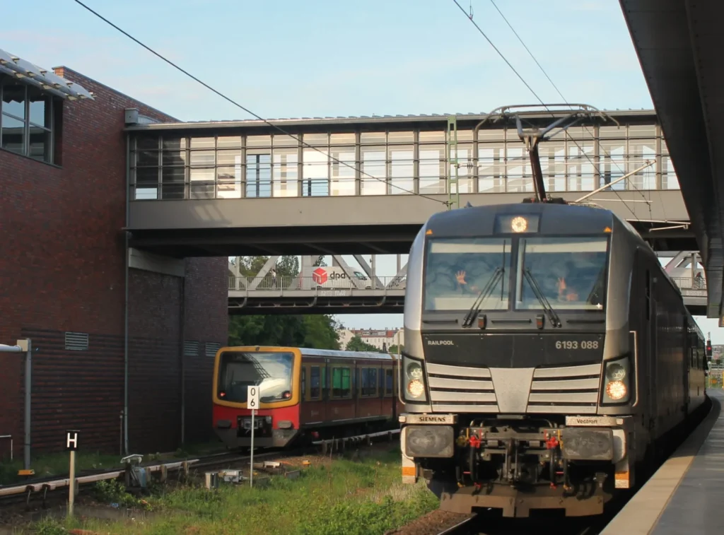 Graue Lokomotive des SJ EuroNight am Bahnhof Gesundbrunnen. Zugführer winken in die Kamera. Am Gleis links daneben eine Berliner S-Bahn.