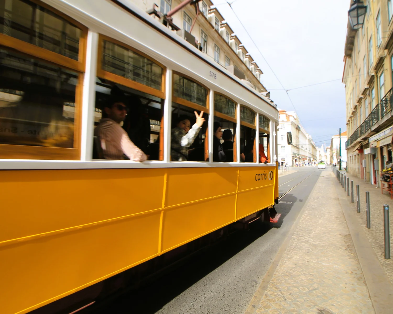 Alte Tram – Vorbeifahrende Straßenbahn in Lissabon. Eine Frau winkt in die Kamera. 