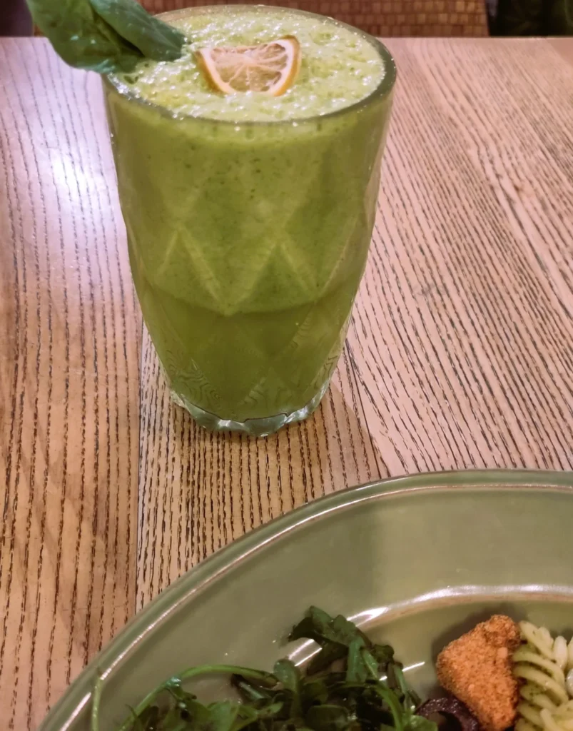 Glas mit grünem Smoothie auf Holztisch hinter Teller in da Terra Restaurant.