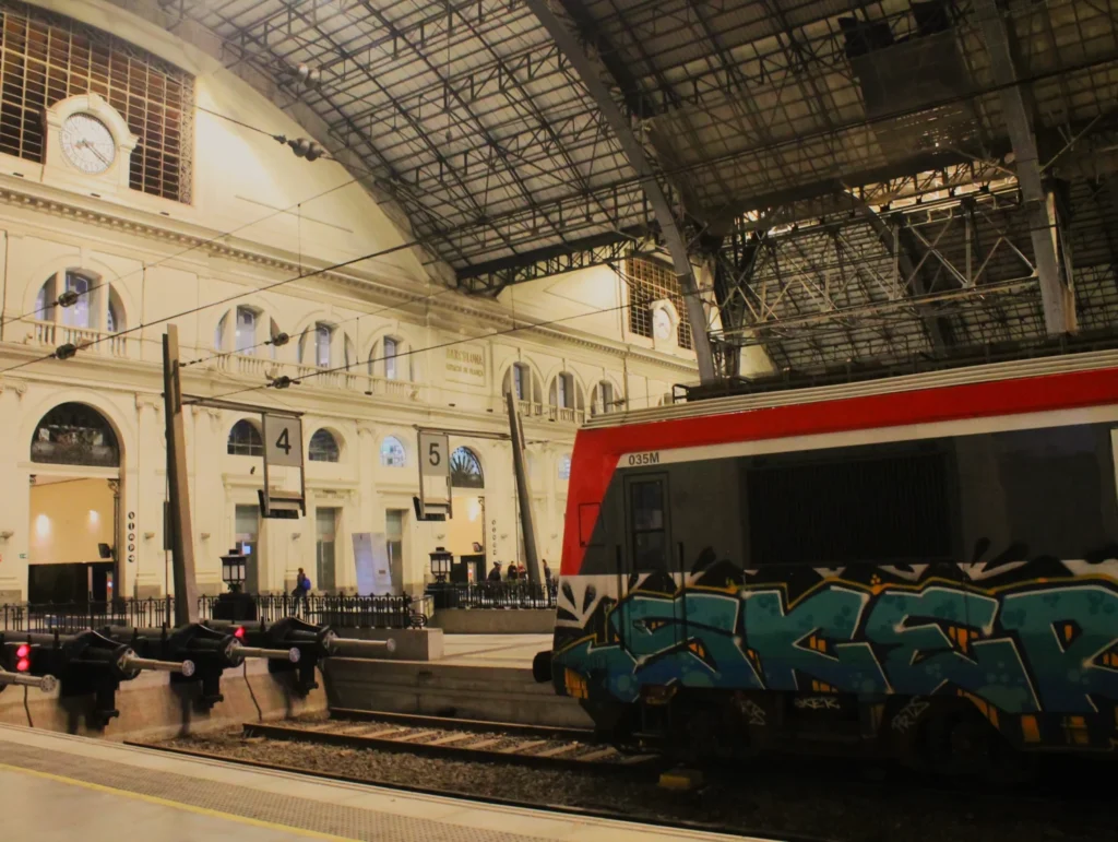 Bahnsteighalle. Bahnhof Barcelona Estacio de França. Vorne ein Zug mit Graffiti im Gleis 4. Metallkonstruktion des Dachs darüber.