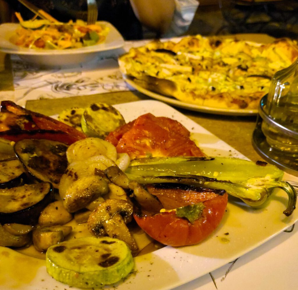 Gegrilltes Gemüse, vegane Pizza und Salat auf Tellern.